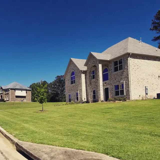 Deep green lawn below a large brick home and blue sky