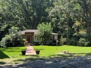 Mowed front lawn and brick walk leading up to a cottage under tall trees