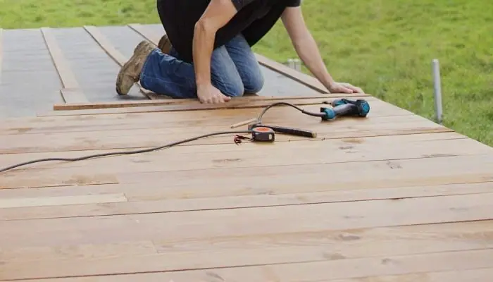 Crew member on their knees laying new boards on a deck frame