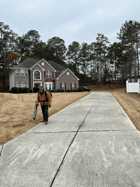 Crew member blowing off a long driveway in front of a brick home