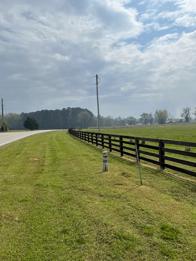 Mowed shoulder along a black board fence and a country road under a wide Georgia sky