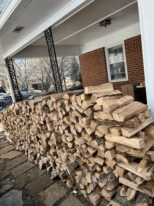 Split firewood stacked along a covered brick carport