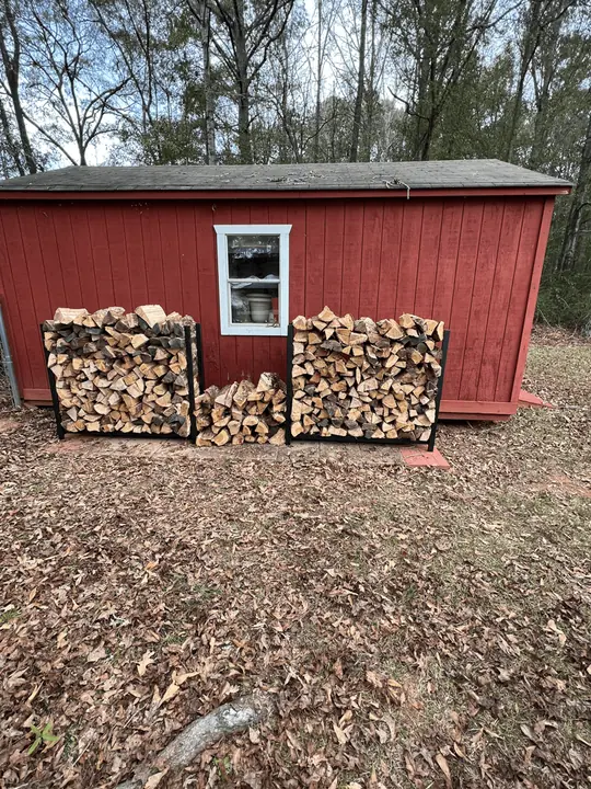 Two stacks of firewood beside a red shed