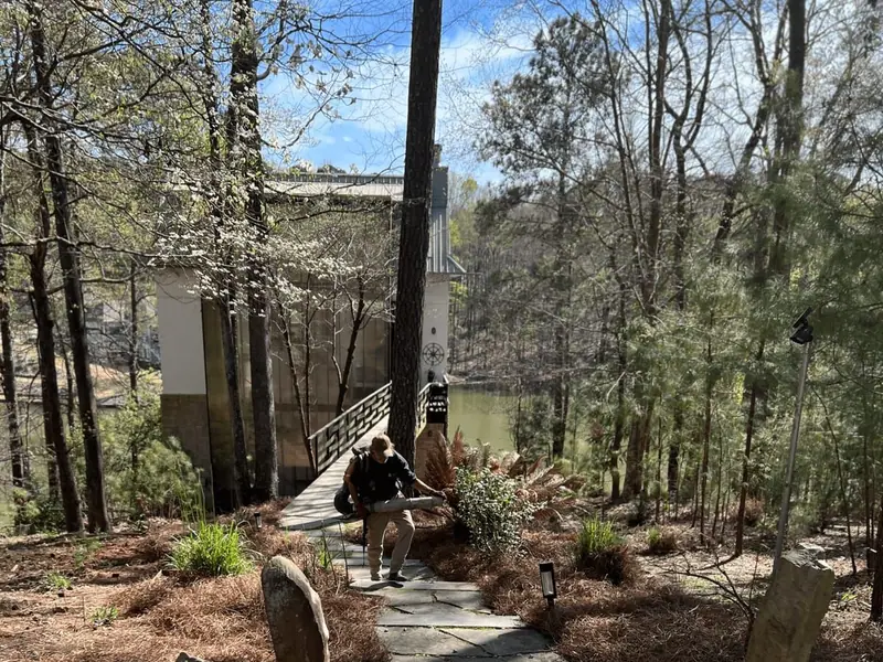 Crew member clearing a stone path between pine straw beds at a lake house