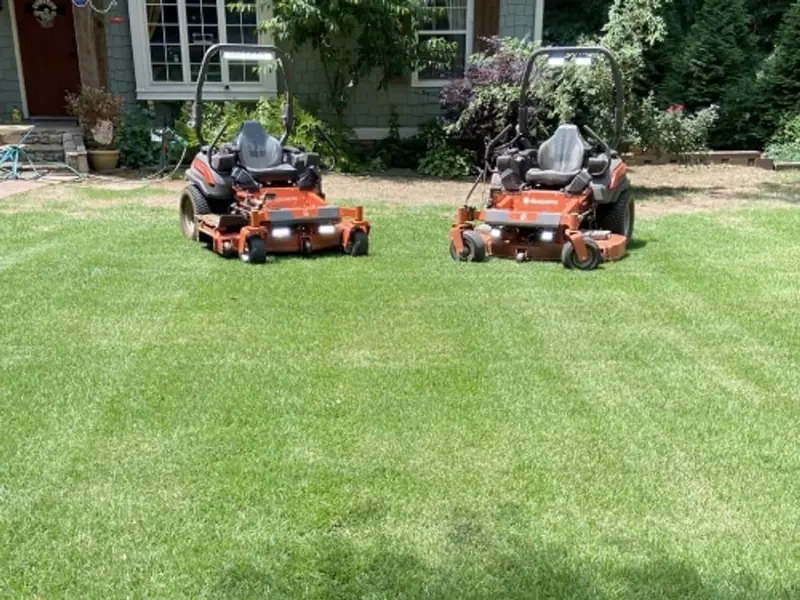 Two orange zero-turn mowers parked on a freshly cut front lawn