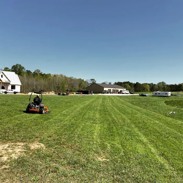 Zero-turn mower cutting an open field with homes in the distance