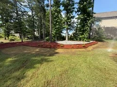 Red mulch bed wrapped around a stand of trees beside a mowed lawn