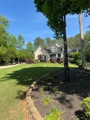 Stone-edged mulch bed under a tree in front of a two-story home