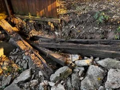 Old landscape timbers and loose rocks along the base of a wooden fence
