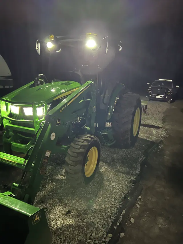 Tractor with its lights on at dusk on a gravel pad