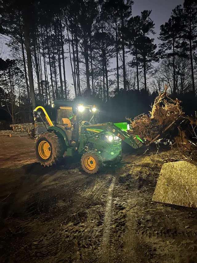 Tractor under work lights pushing a root ball on a cleared lot