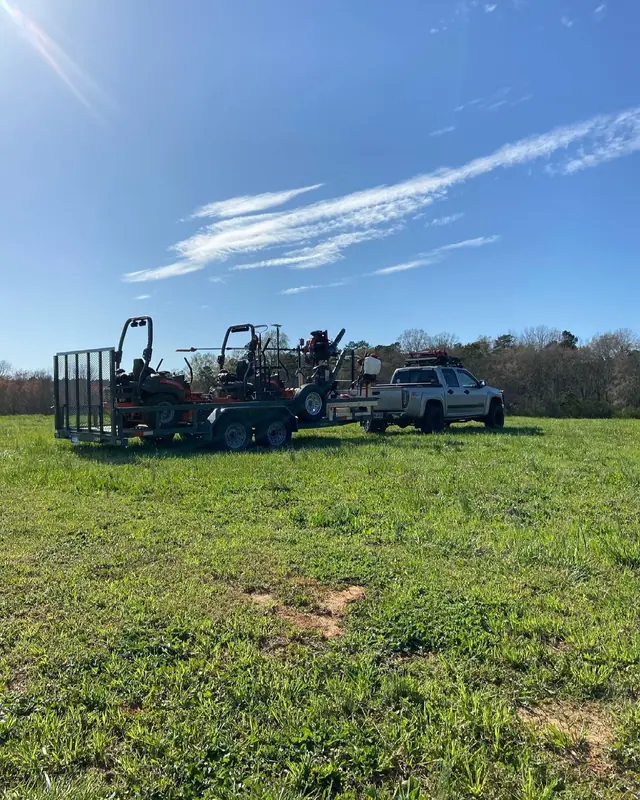 Equipment trailers and a pickup parked in an open field under a blue sky