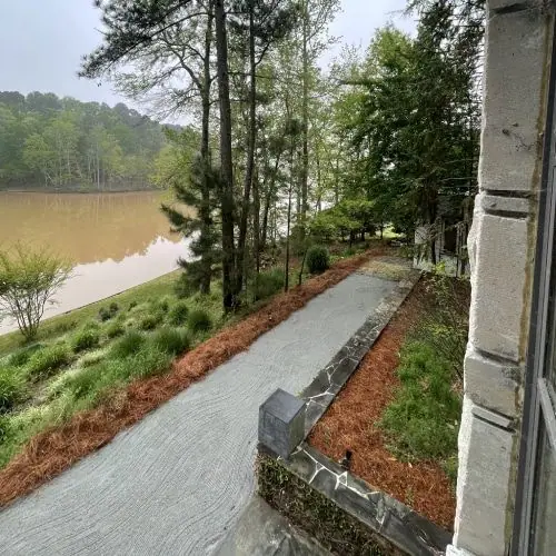 Walkway edged with a stacked stone wall and fresh mulch beds above a lake